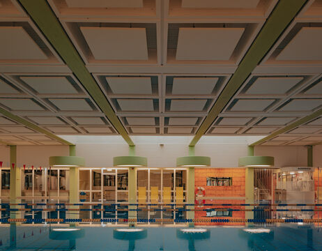 Hallenbad mit blauem Wasser, Glasbarrieren und einer modernen Decke mit quadratischen Paneelen.