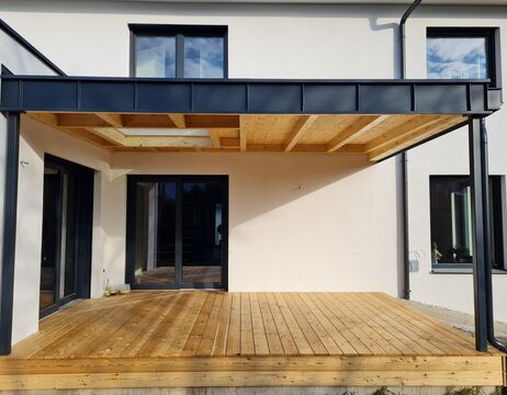 Moderner Innenhof mit Holzterrasse und einer schwarzen Pergola mit Metallrahmen, die an ein helles Haus angebaut ist.